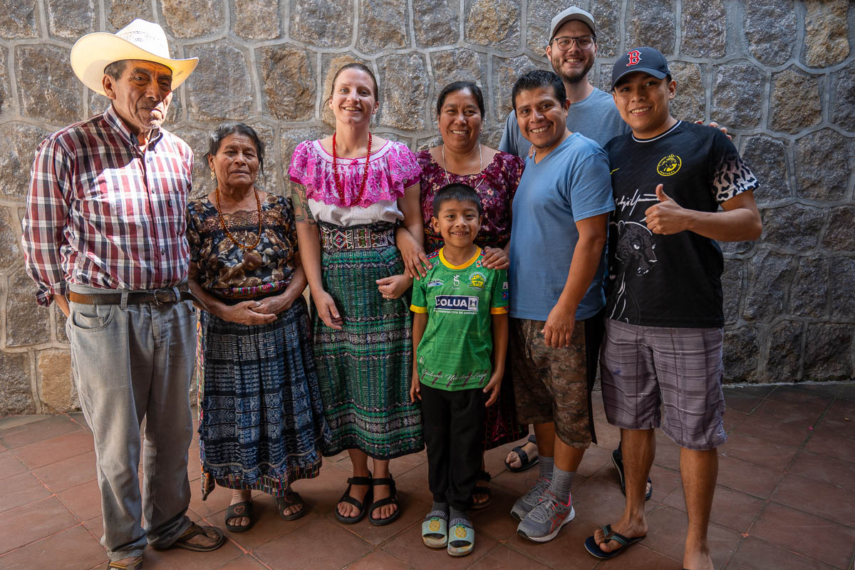 Couple smiling with a Guatemalan family with a rock wall in the background in San Pedro, Guatemala