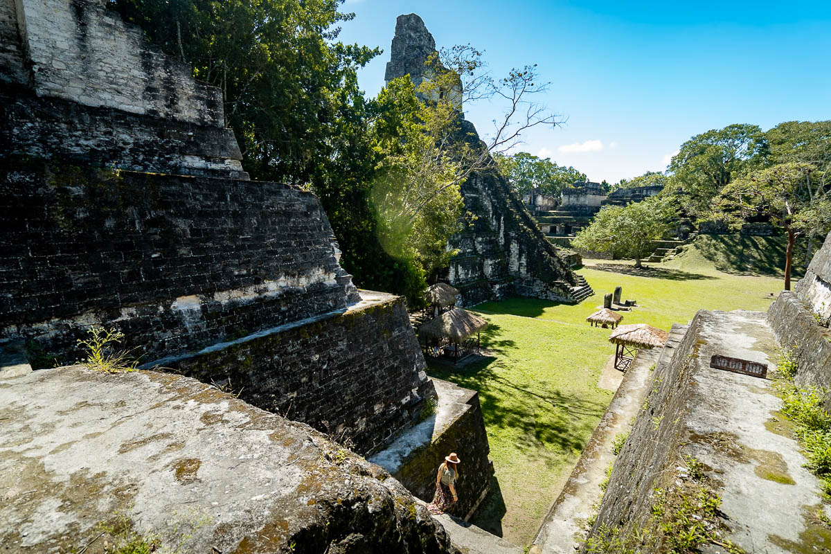 Woman walking down steps with temples in the background in Tikal National Park in Guatemala