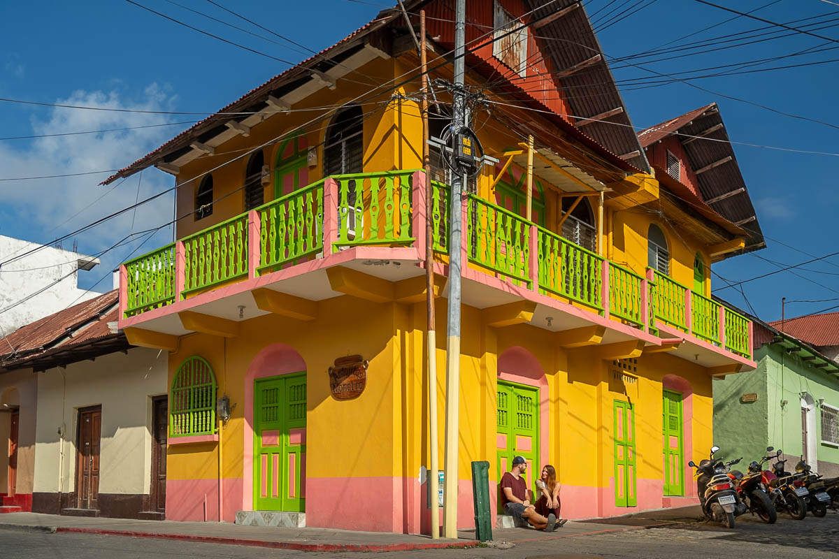 Couple sitting on a curb in front of a colorful building in Flores, Guatemala