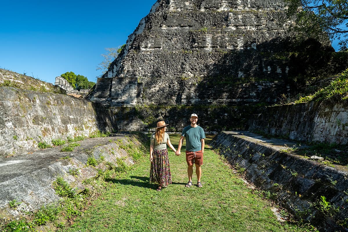 Couple holding hands in between stone ruins near Temple I in the Grand Plaza in Tikal National Park in Guatemala