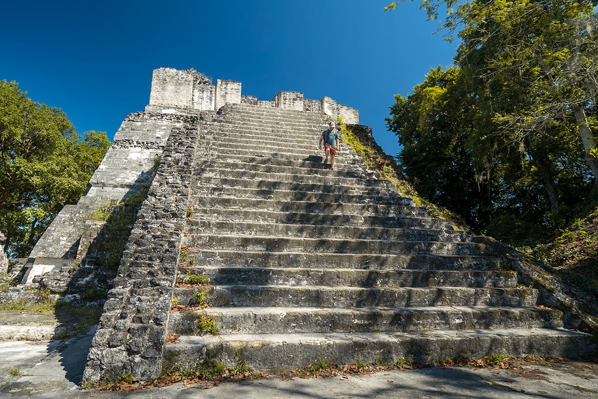 Man walking down stairs on a stone temple at the Grand Plaza of Tikal National Park in Guatemala