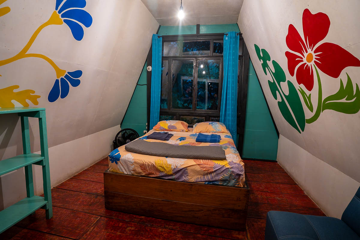 Bed in an A-frame cabin with colorful paintings on the wall at Greengos Hotel near Semuc Champey, Guatemala