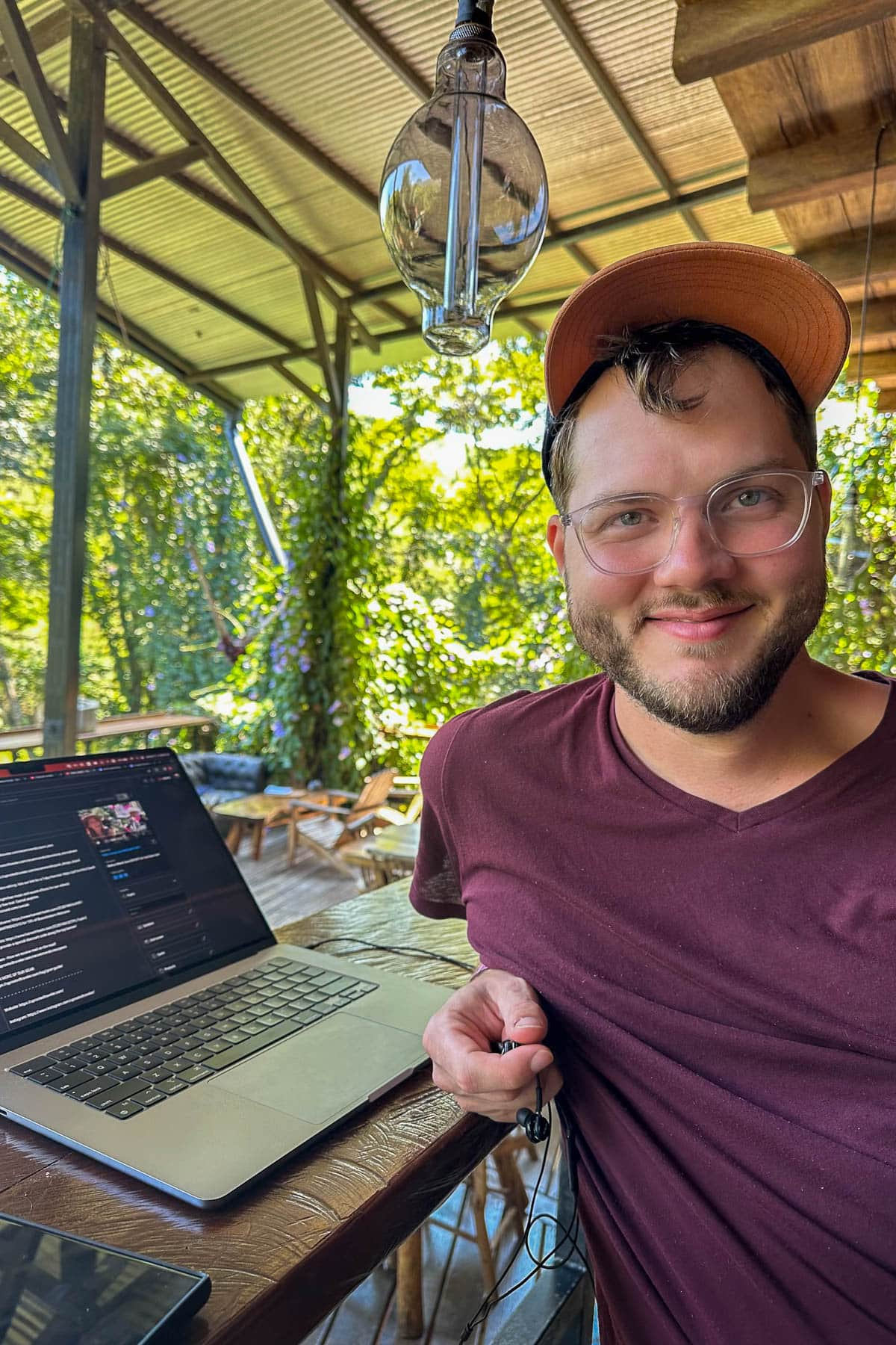 Man sitting with a laptop at a wooden counter with jungle in the background at Greengos Hotel near Semuc Champey, Guatemala