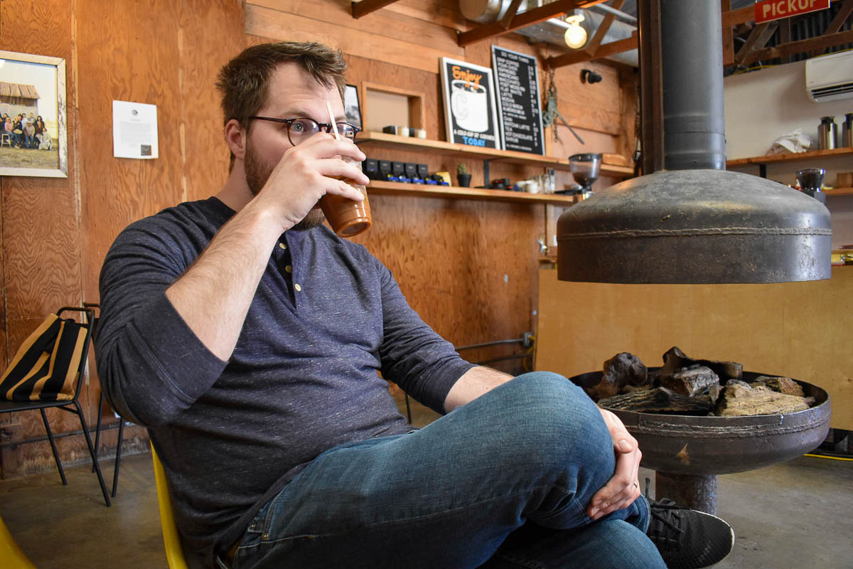 Man drinking an iced coffee with a fireplace in the background at Bitter Sugar Coffee in Marfa, Texas