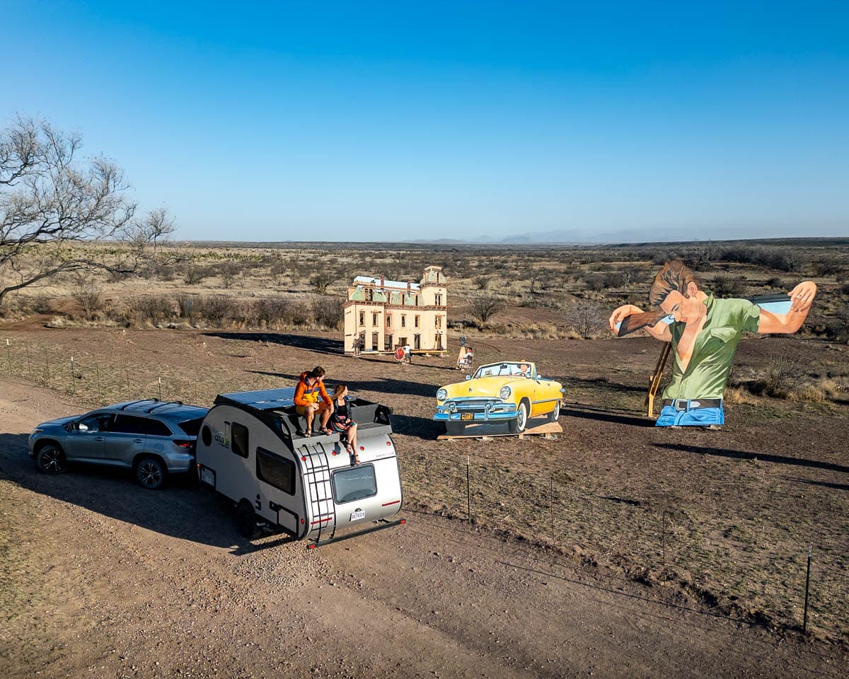 Couple sitting on top of a Safari Condo Alto F1743 Expedition with a cut out of James Dean in the background in Marfa, Texas