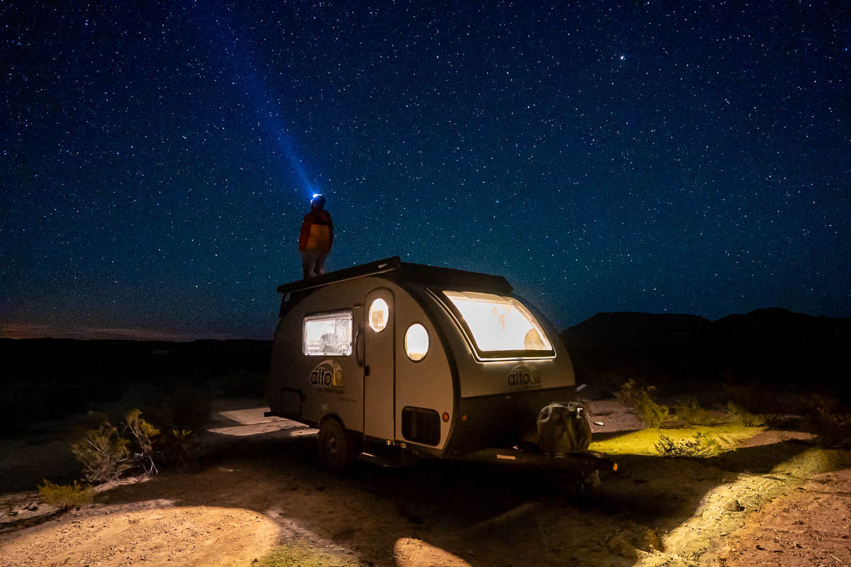 Man standing on top of a Safari Condo Alto F1743 Expedition trailer with stars in the night sky near Big Bend National Park in Texas