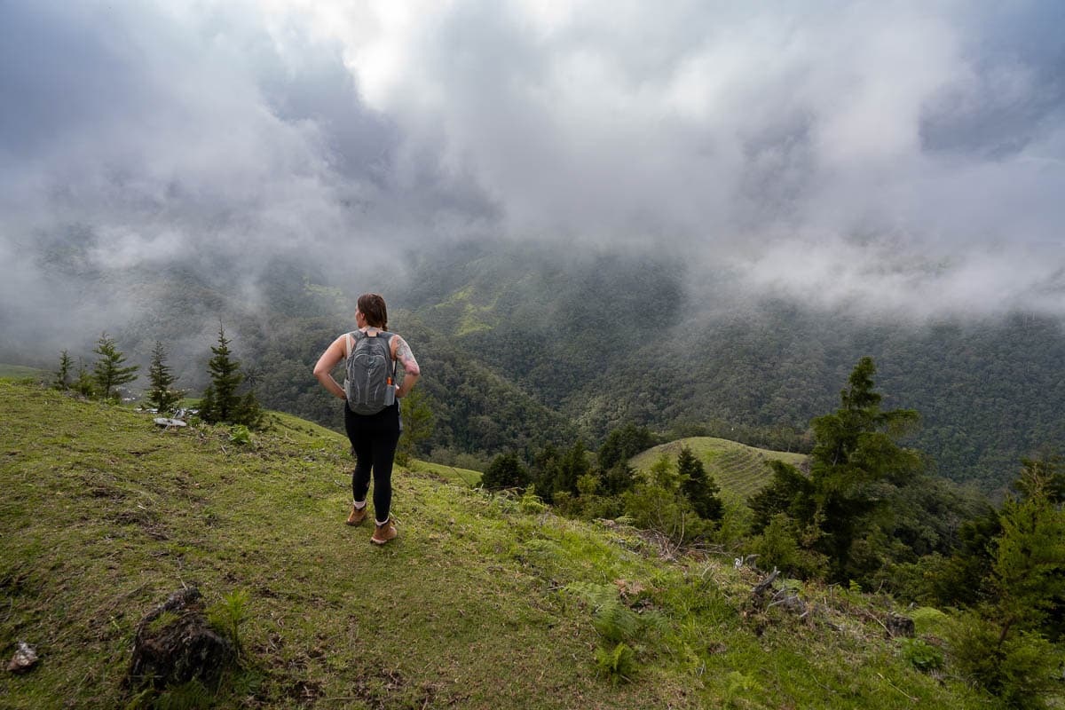 Woman standing along the Cerro Morrogacho trail with pastures downhill and low handing clouds in the Cocora Valley near Salento, Colombia