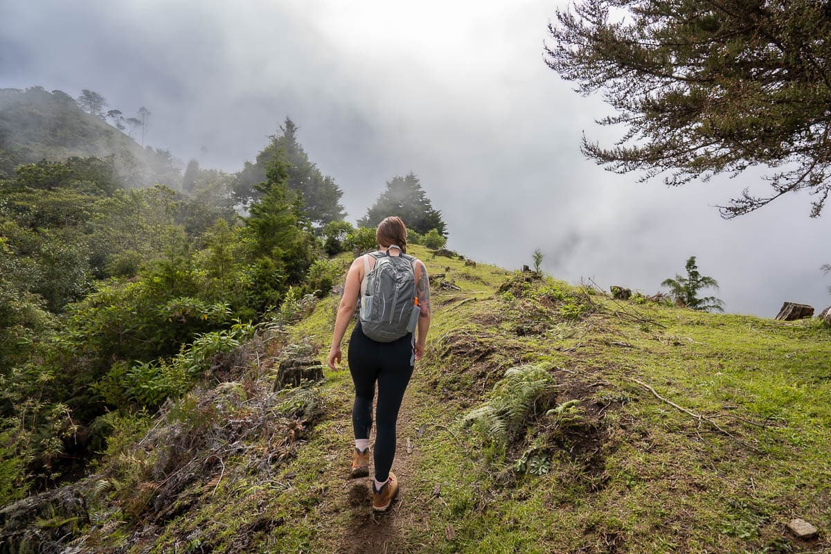 Woman climbing up a steep, grassy hill with low-hanging clouds along the Cerro Morrogacho trail in Cocora Valley near Salento, Colombia