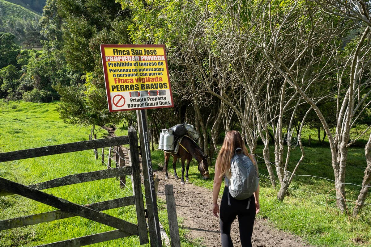 Woman walking past a private property sign along the Cerro Morrogacho trail in the Cocora Valley near Salento, Colombia