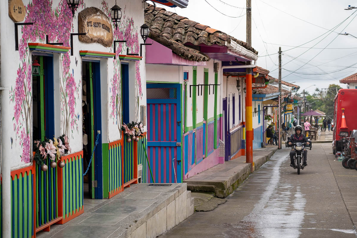 Man on a scooter driving past colorful buildings in Salento, Colombia