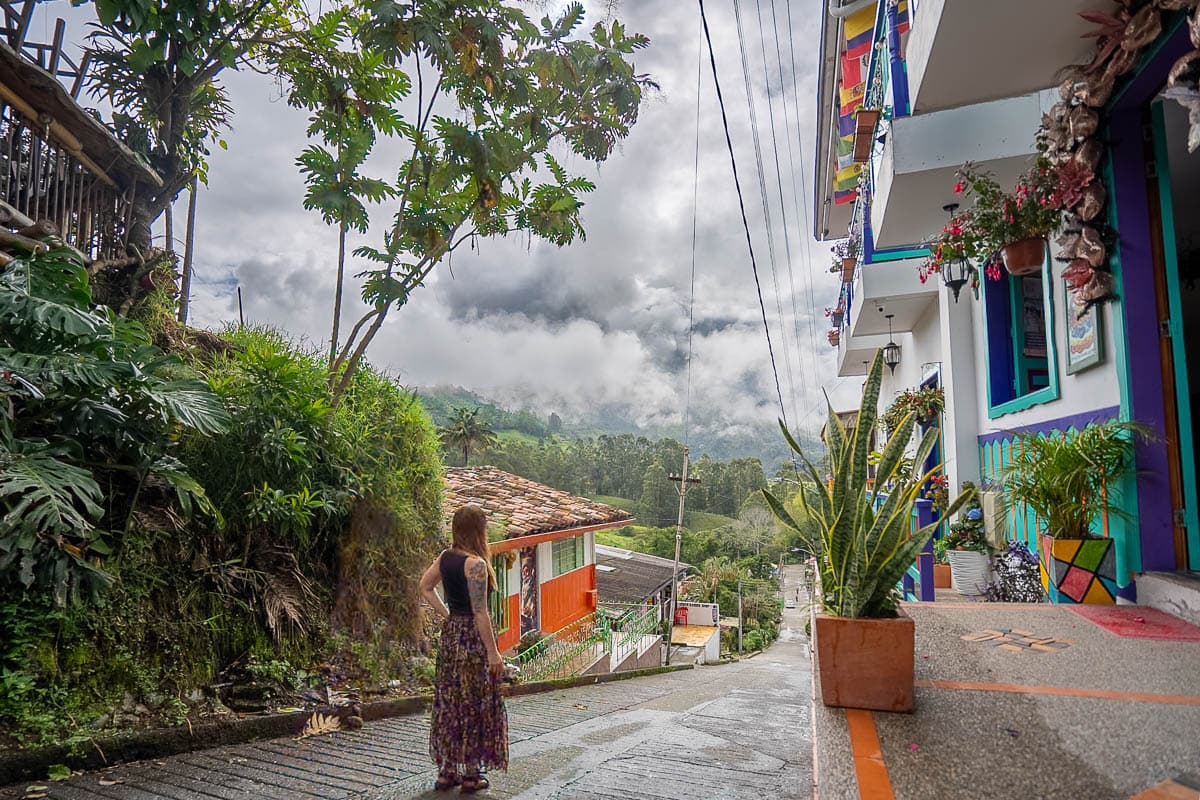 Woman standing along a street with colorful buildings and mountains in the background near Salento, Colombia