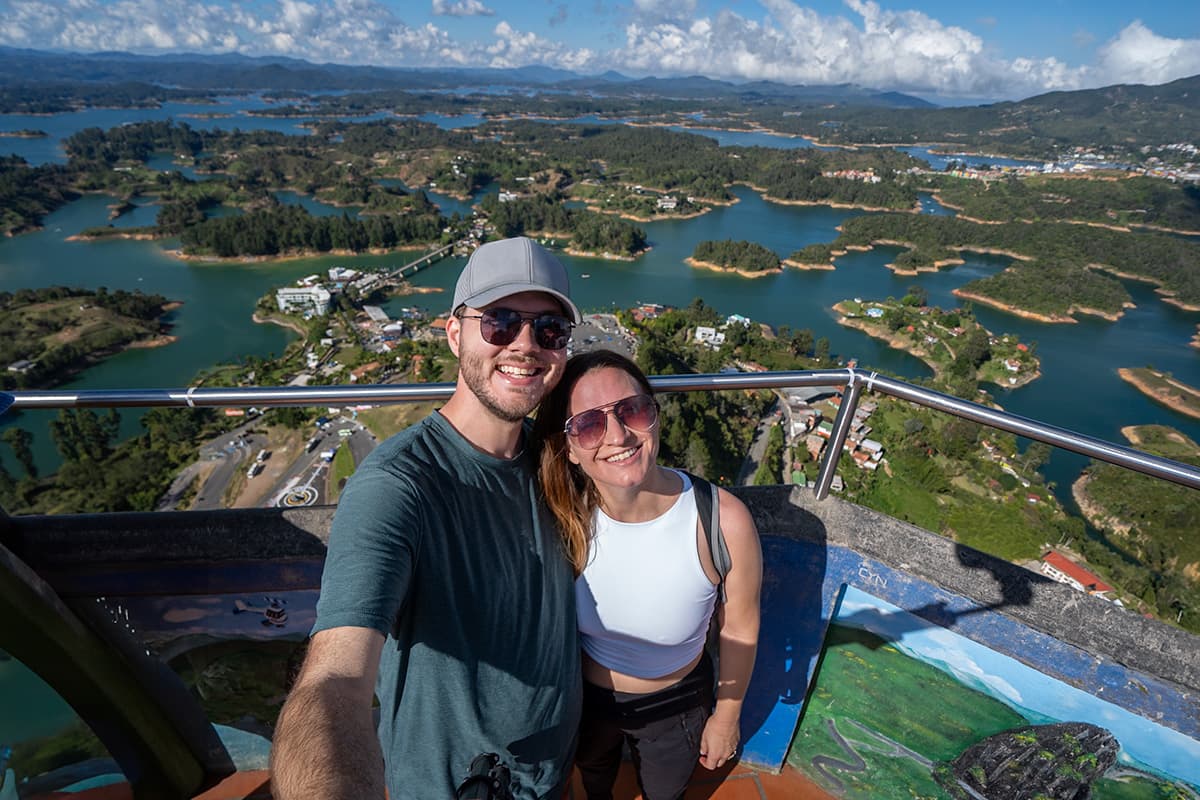 Couple smiling at the lookout for The Rock with Guatape-Penol Reservoir in the background in Guatape, Colombia