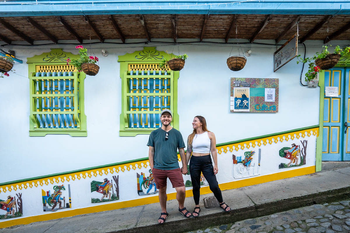 Couple holding hands in front of colorful zócalos on a cobblestone street in Guatape, Colombia