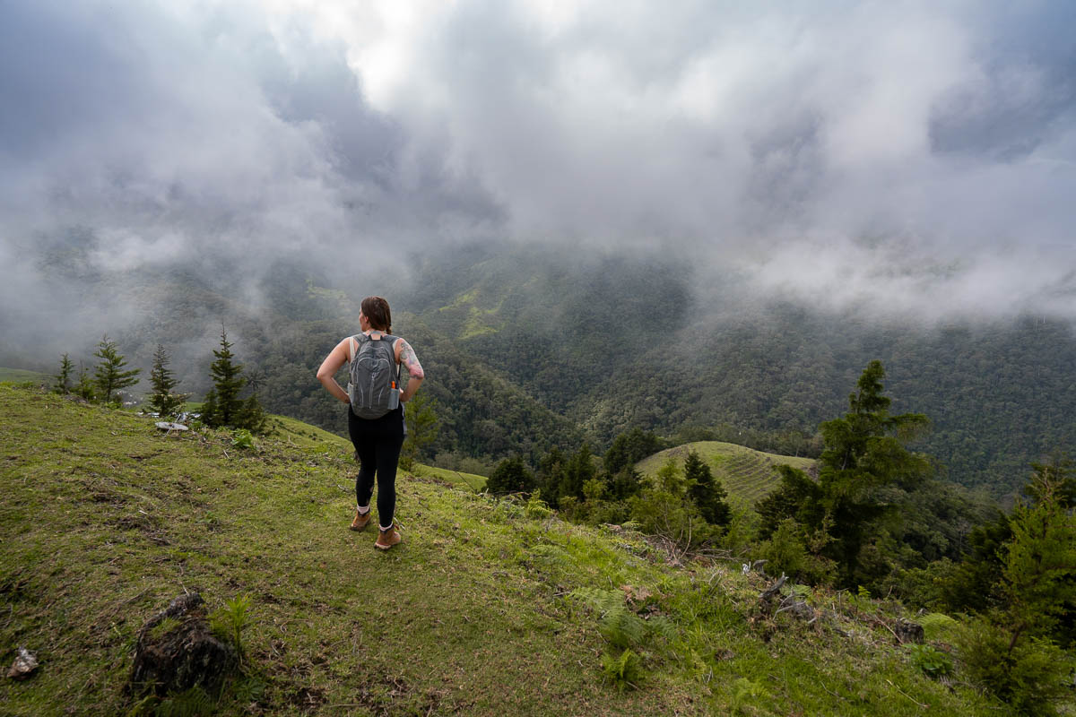 Woman standing on a hillside with low-hanging clouds in the background in the Cocora Valley in Salento, Colombia