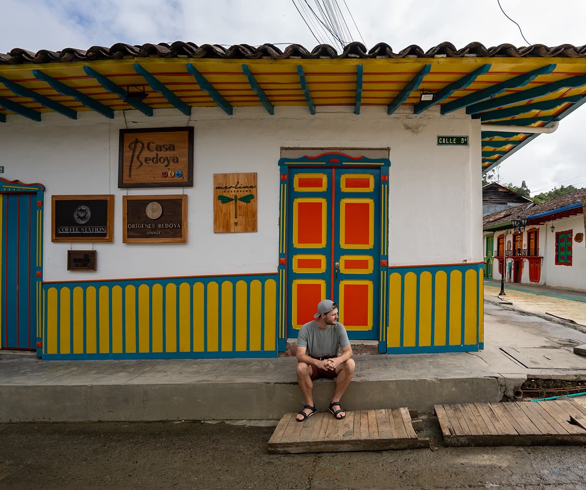 Man sitting on a curb in front of a colorful building in Saento, Colombia