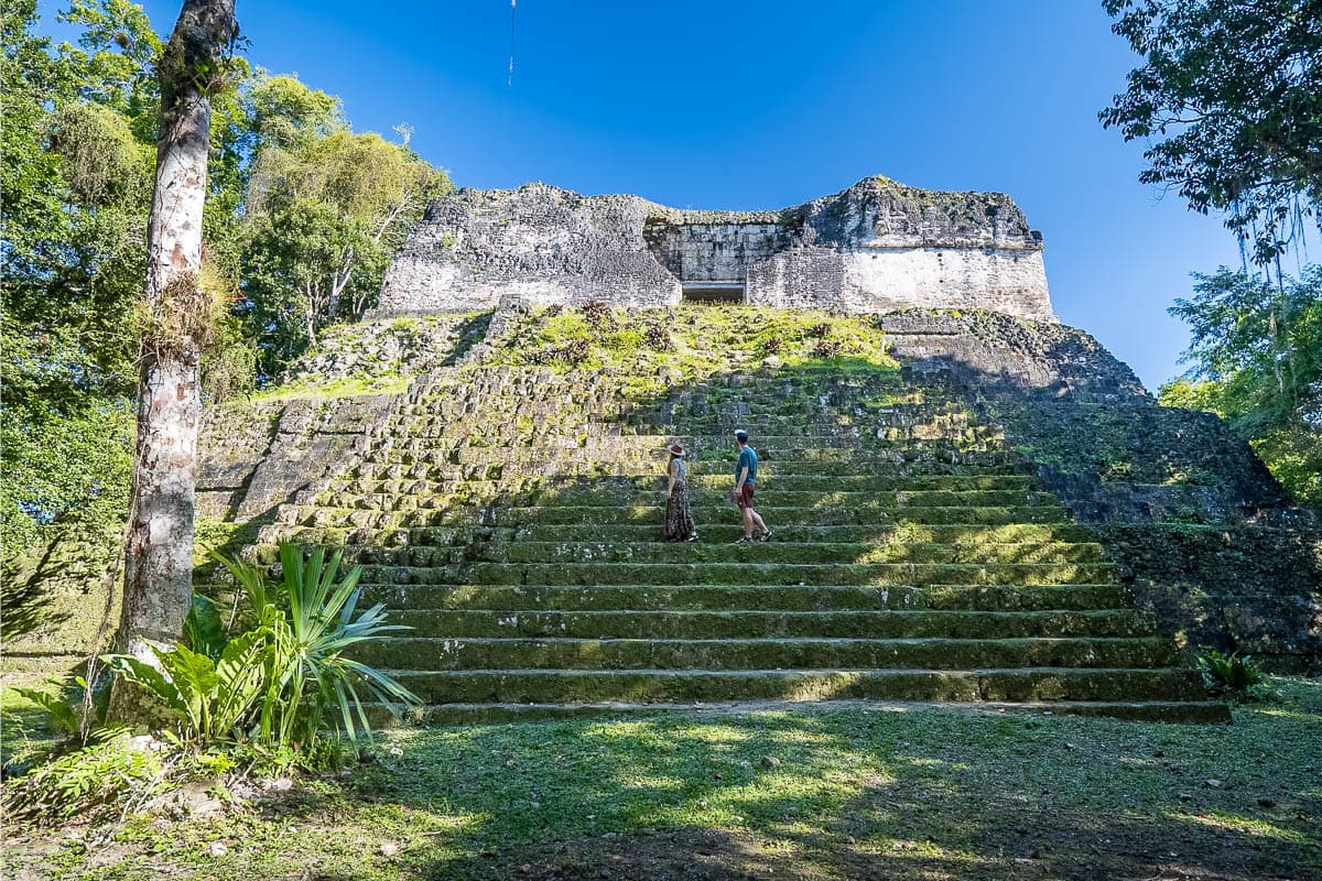 Couple walking across mossy stairs of a temple at the ancient Mayan ruins of Tikal in Guatemala