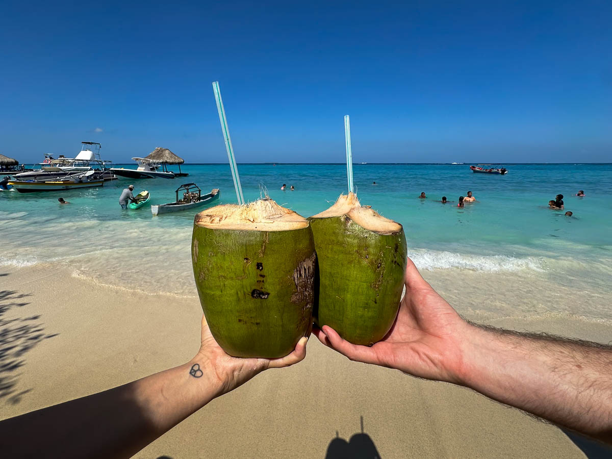 Couple holding fresh coconuts in front of Playa Libre on Isla Grande in Colombia