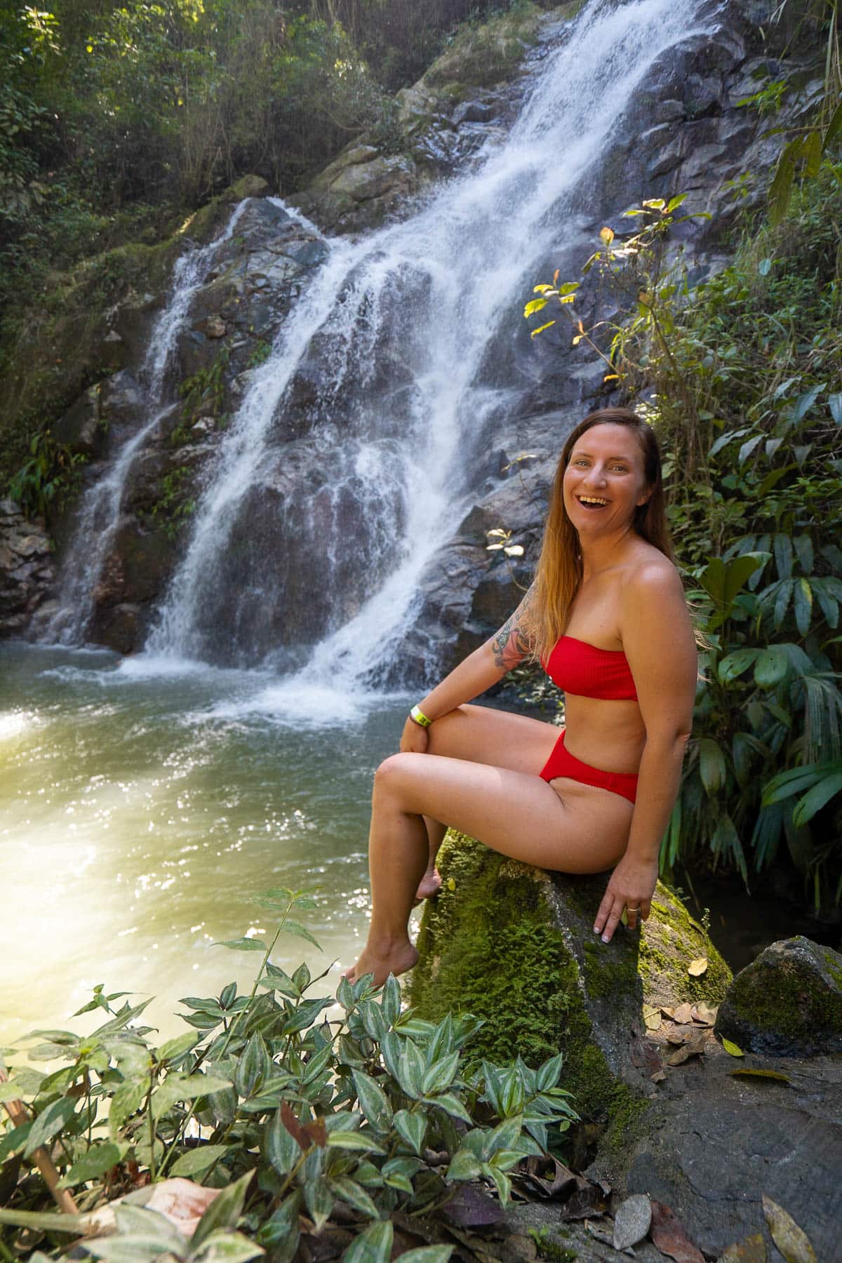 Smiling woman sitting on a rock at the Mirinka Waterfall in the background in Minca, Colombia