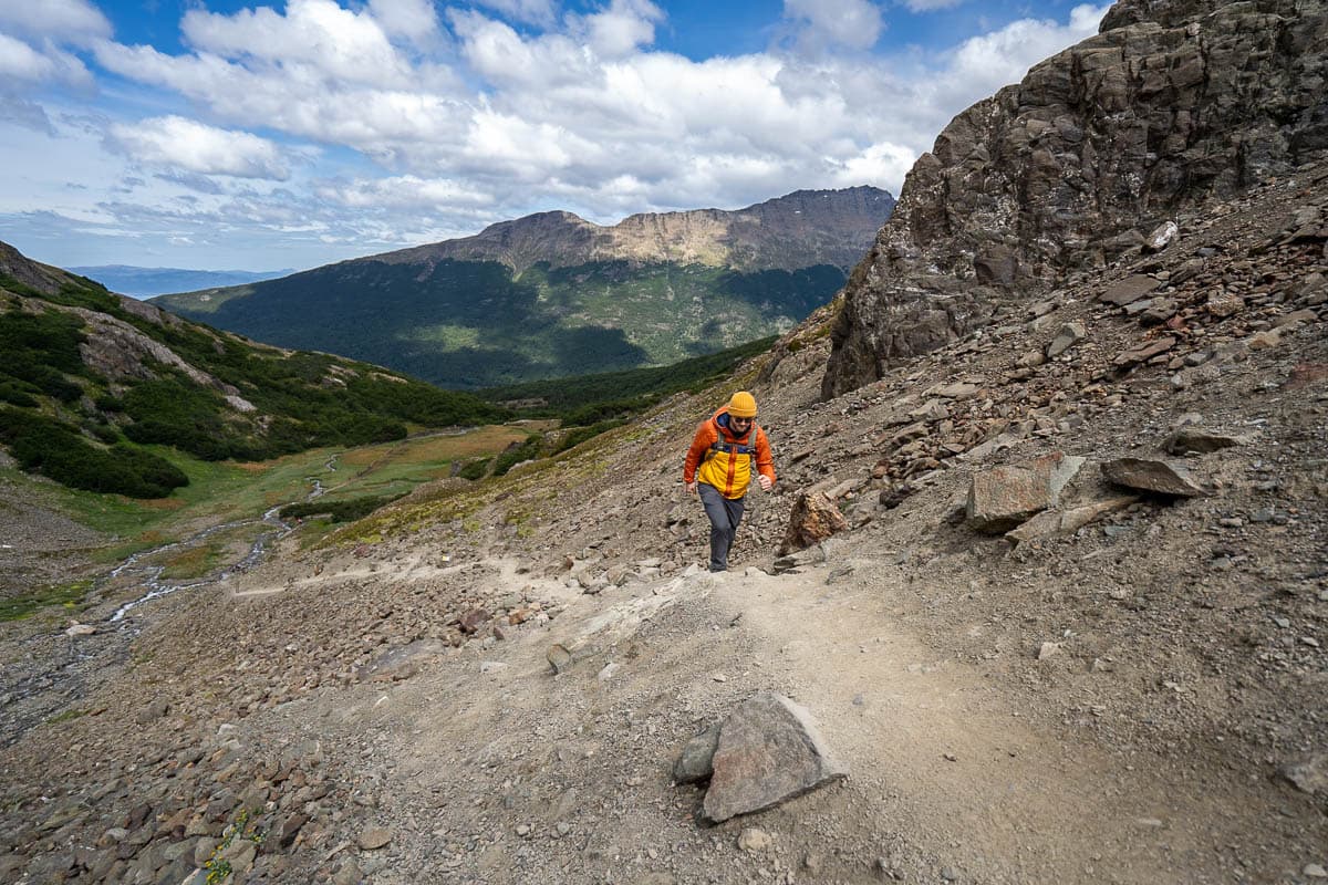 Man hiking up a steep scree field along Laguna de los Tempanos trail with mountains in the background of Ushuaia, Argentina