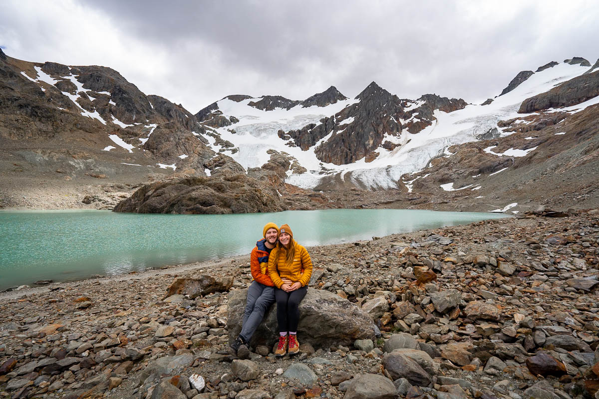 Couple sitting on a rock in front of Laguna de los Tempanos with mountains in the background in Ushuaia, Argentina