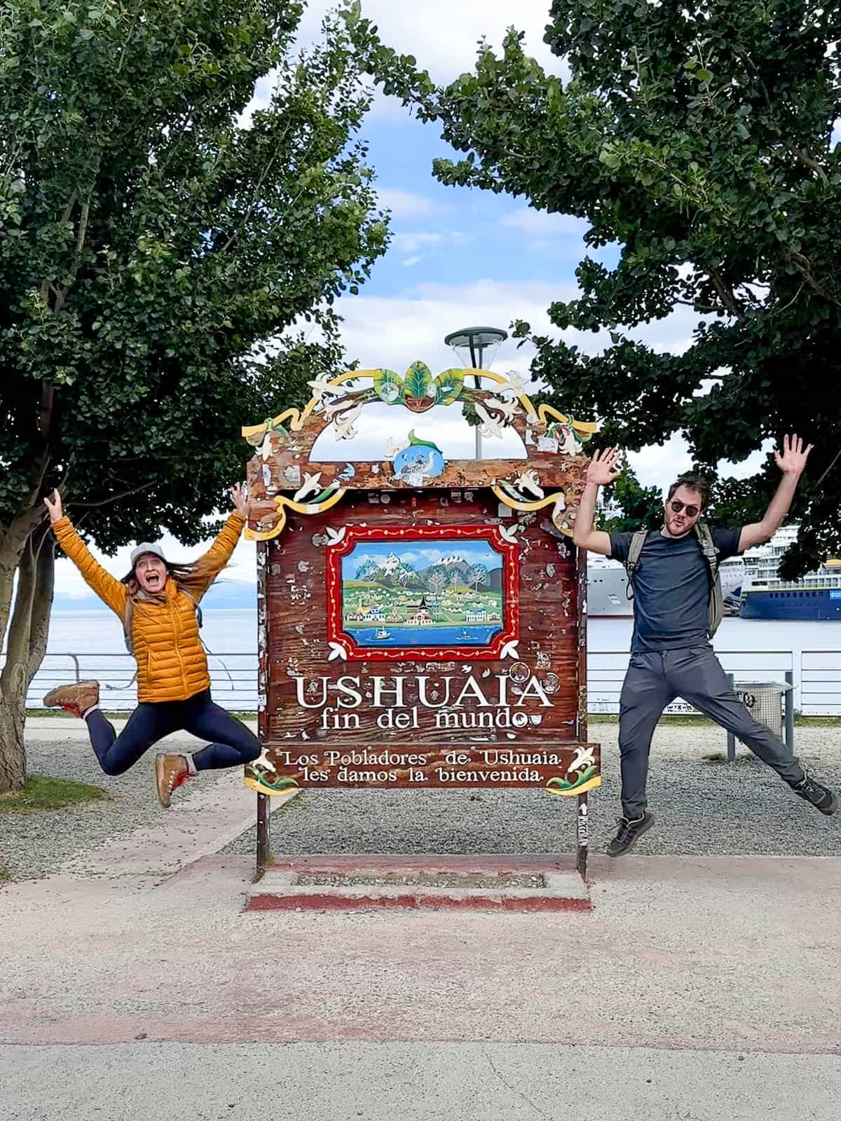 Couple jumping by the Fin del Mundo sign in the port of Ushuaia, Argentina