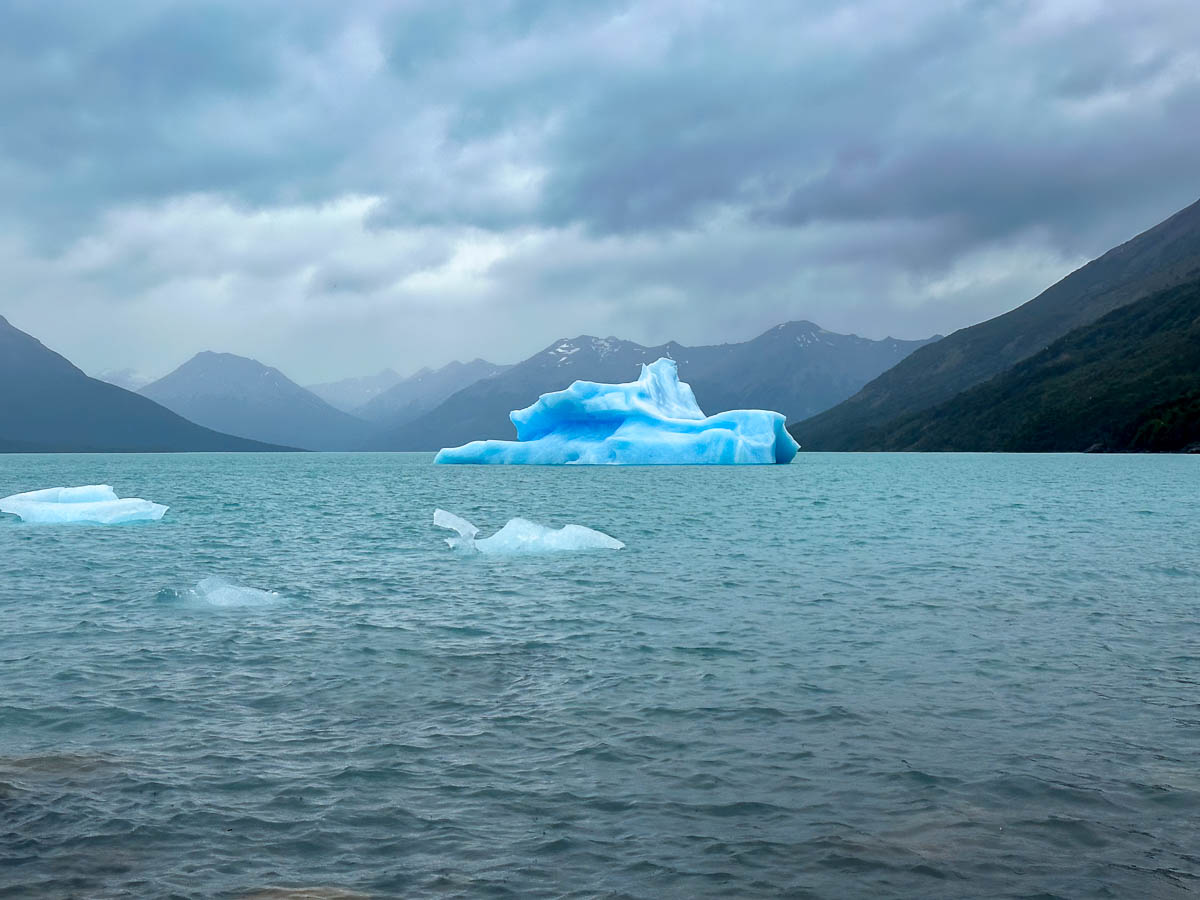 Blue iceberg floating in Lago Argentina surrounded by mountains along Sendero de la Costa in Los Glaciares National Park near El Calafate, Argentina