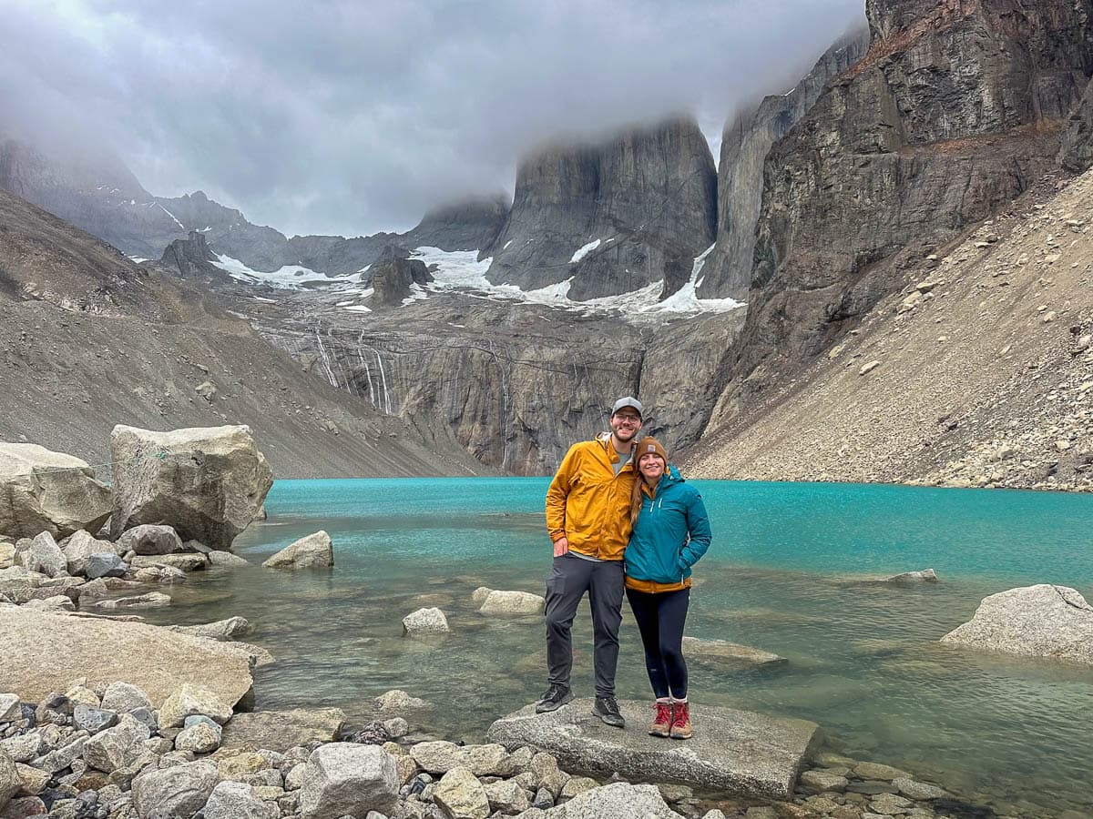 Couple standing in front of Lago Torres with clouds covering the towers of Torres del Paine along the W trek in Torres del Paine National Park in Chilean Patagonia