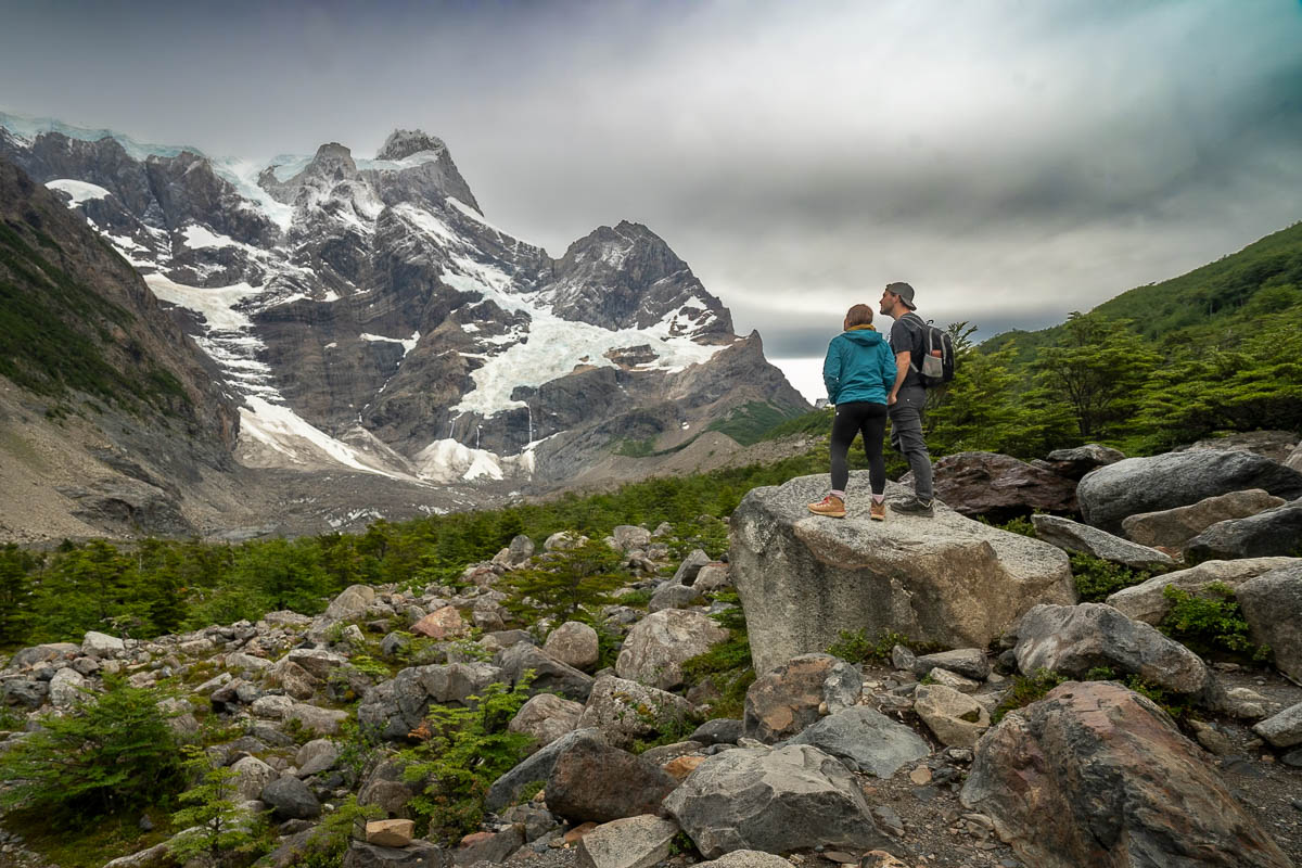 Couple standing on top of a boulder looking at the French Glacier on Paine Grande mountain in the French Glacier along the W Trek in Torres del Paine National Park in Chilean Patagonia
