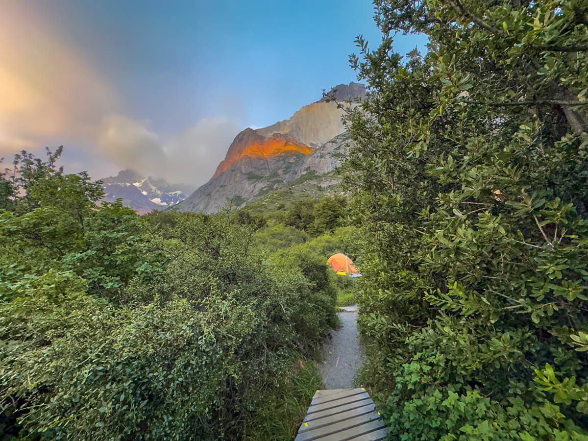Tent at the end of a pathway with mountains with alpine glow at sunrise at Refugio Cuernos in Torres del Paine National Park in Chilean Patagonia