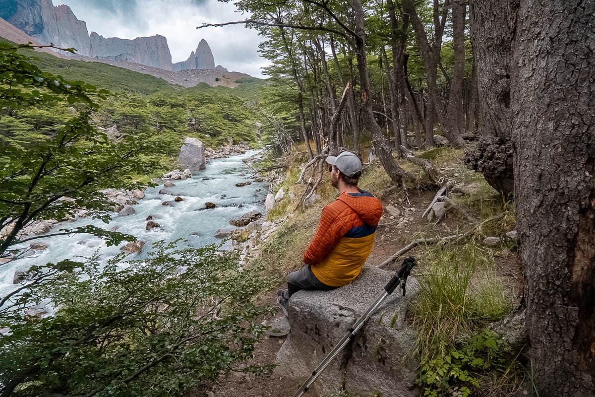 Man sitting on a boulder and looking at Rio del Frances with the French Valley in the background along the W Trek in Chilean Patagonia