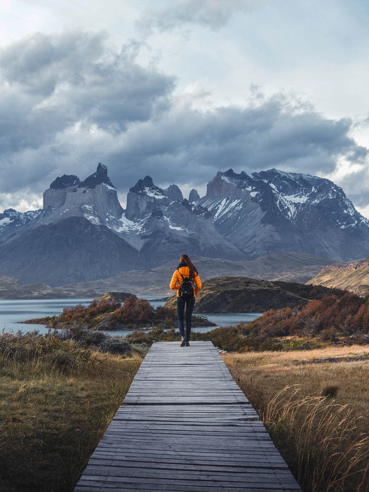 Woman standing on the Lake Pehoe boardwalk with the Cordillera del Paine mountains in the background in Torres del Paine National Park in Chilean Patagonia