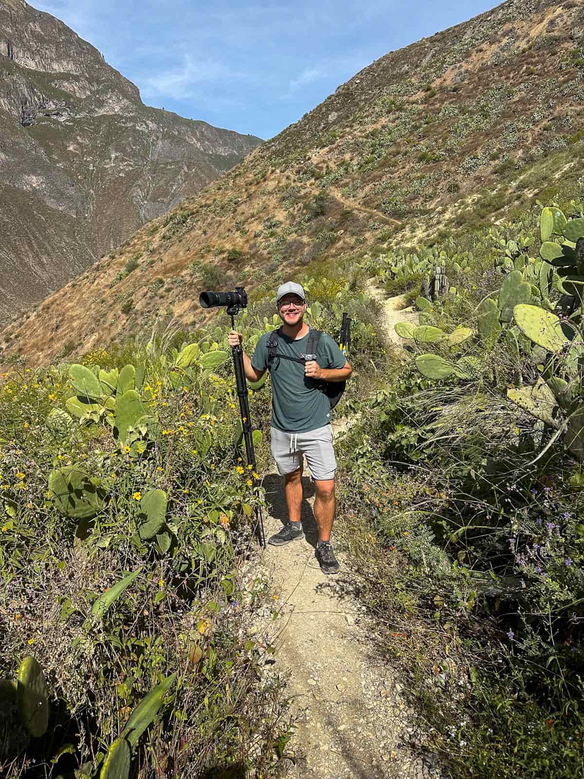 Smiling man holding a tripod and camera surrounded by greenery along the Colca Canyon trail in Peru