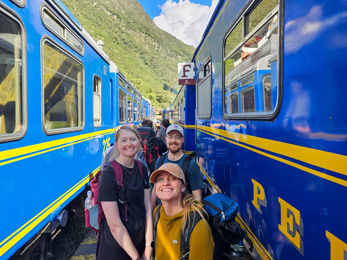 Three hikers smiling in between two PeruRail trains in Ollytantambo, Peru