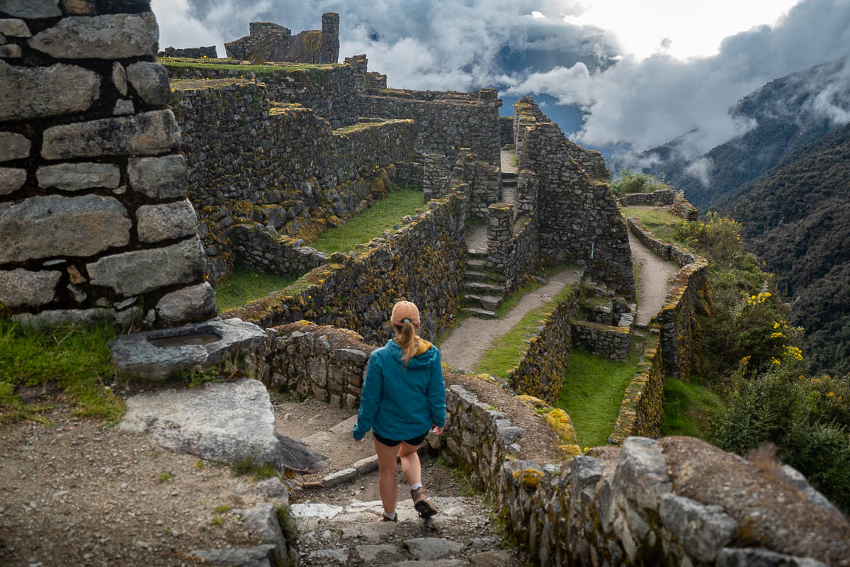 Woman walking down stairs at Sayacmarca ruins with mountains and moody clouds in the background along the Inca Trail in Peru