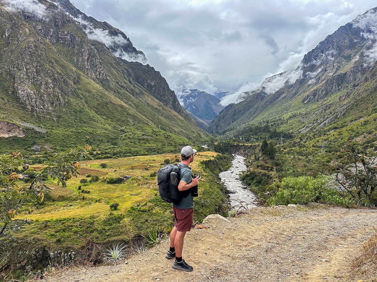 Man with a backpack looking at Rio Urubamba with the Andes Mountains in the background along the Inca Trail in Peru