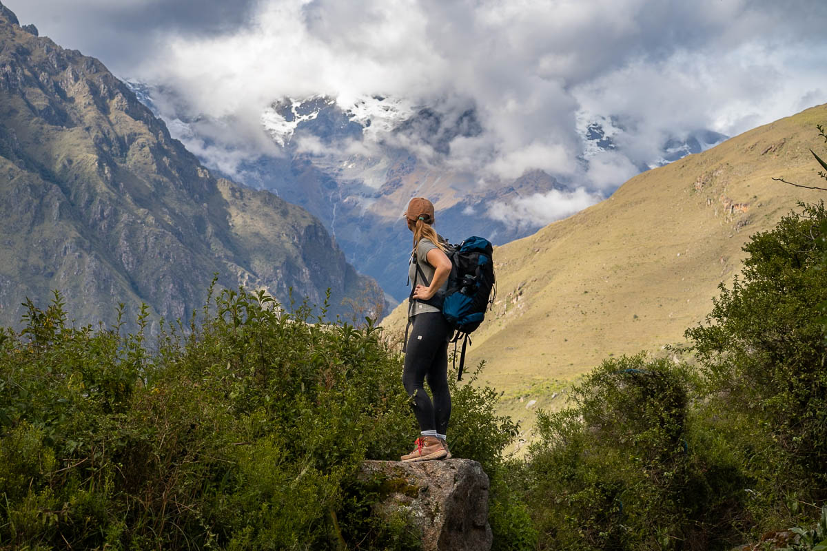 Woman standing on a boulder with Andes Mountains in the background along the Inca Trail in Peru