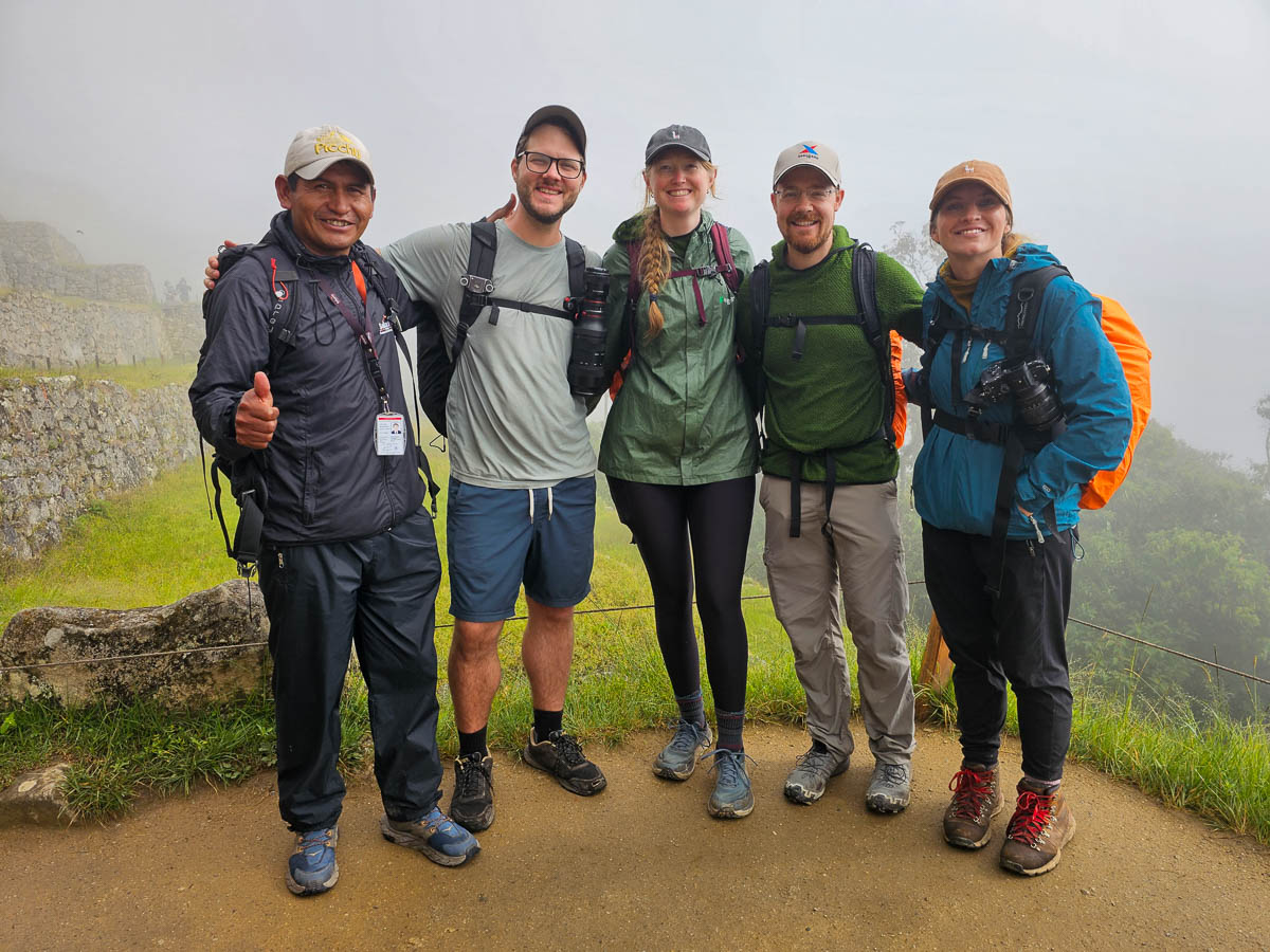Four hikers smiling with their Inca Trail guide at Machu Picchu in Peru