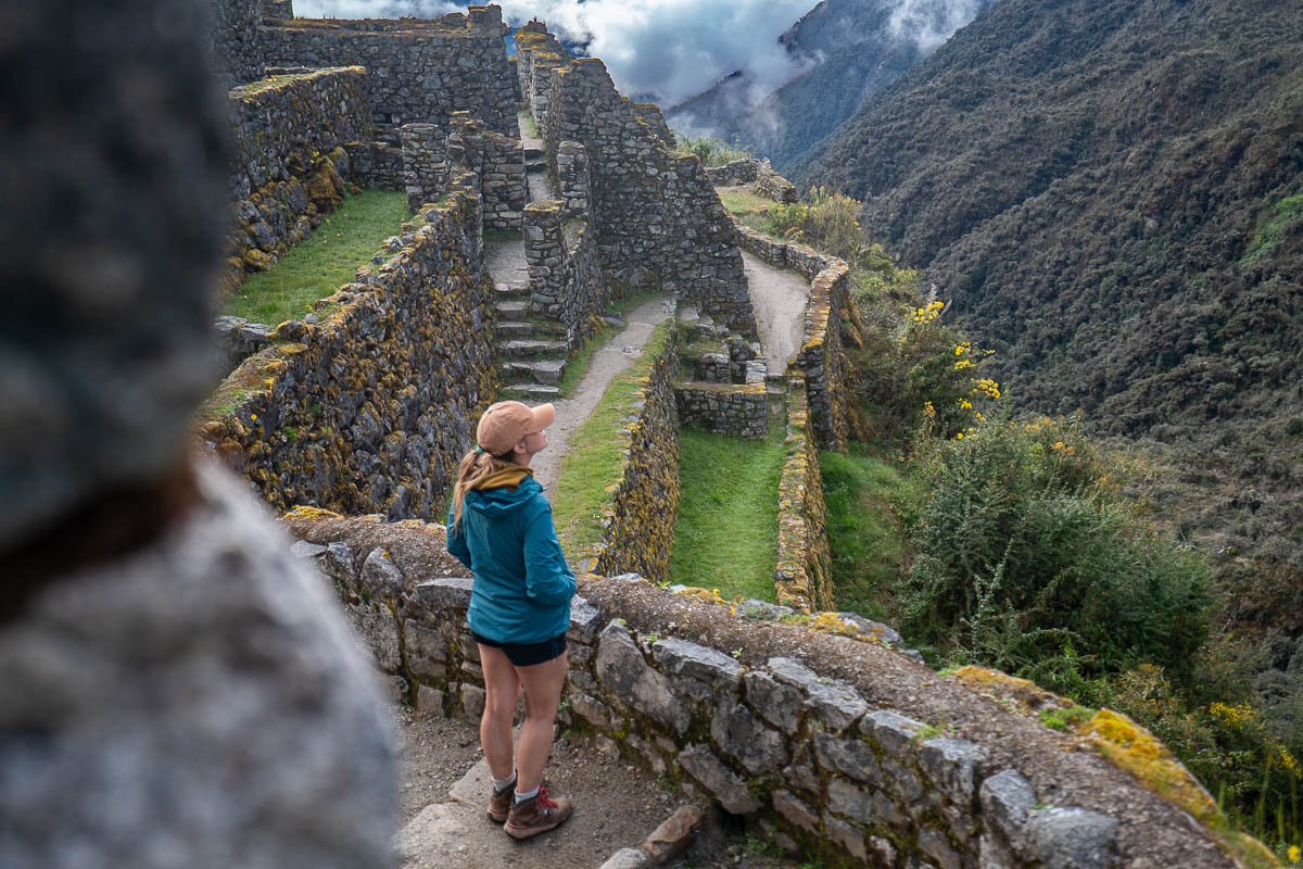 Woman standing on the staircase of Sayacmarca ruins with mountains in the background along the Inca trail in Peru
