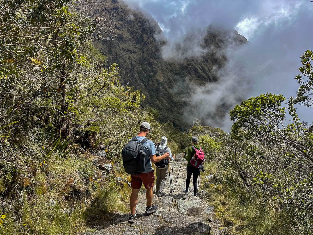 Three hikers walking down stone stairs with Andes mountains in the background along the Inca Trail in Peru