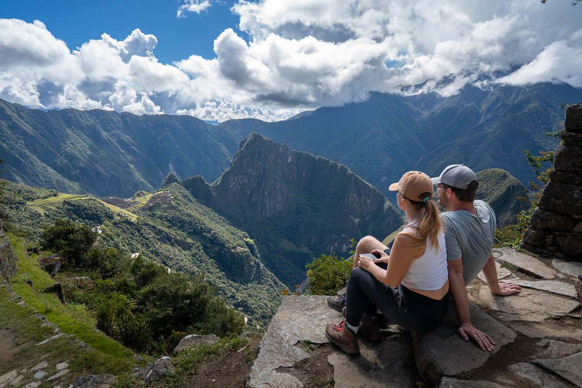 Couple sitting on a staricase looking at Machu Picchu in the background at the Sungate in Peru