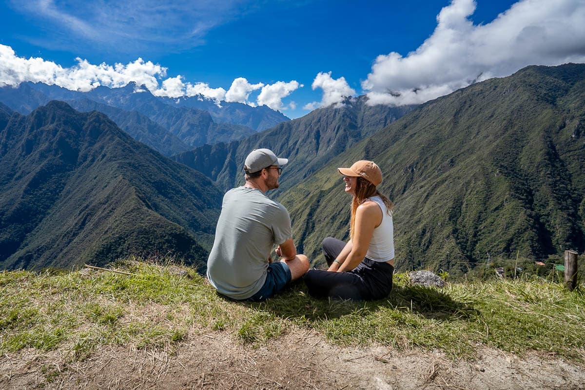 Couple sitting on a cliff at the Intipata ruins with Andes Mountains in the background along the Inca Trail in Peru