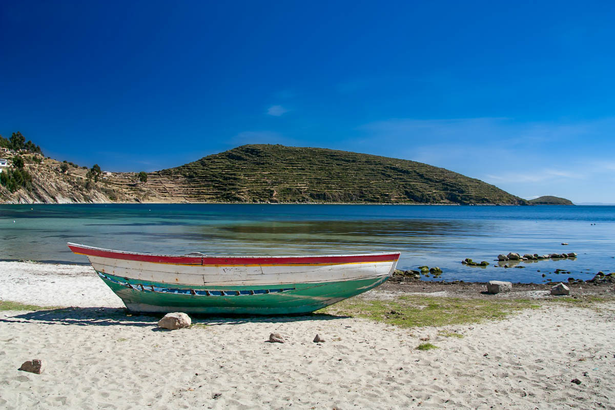 Painted boat on a sandy beach with mountains in the background in Isla del Sol, Bolivia