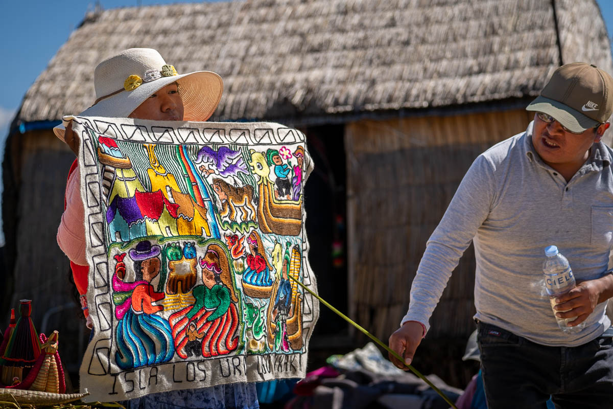 Woman holding an embroidered textile as a man points to it on the Uros islands near Puno, Peru
