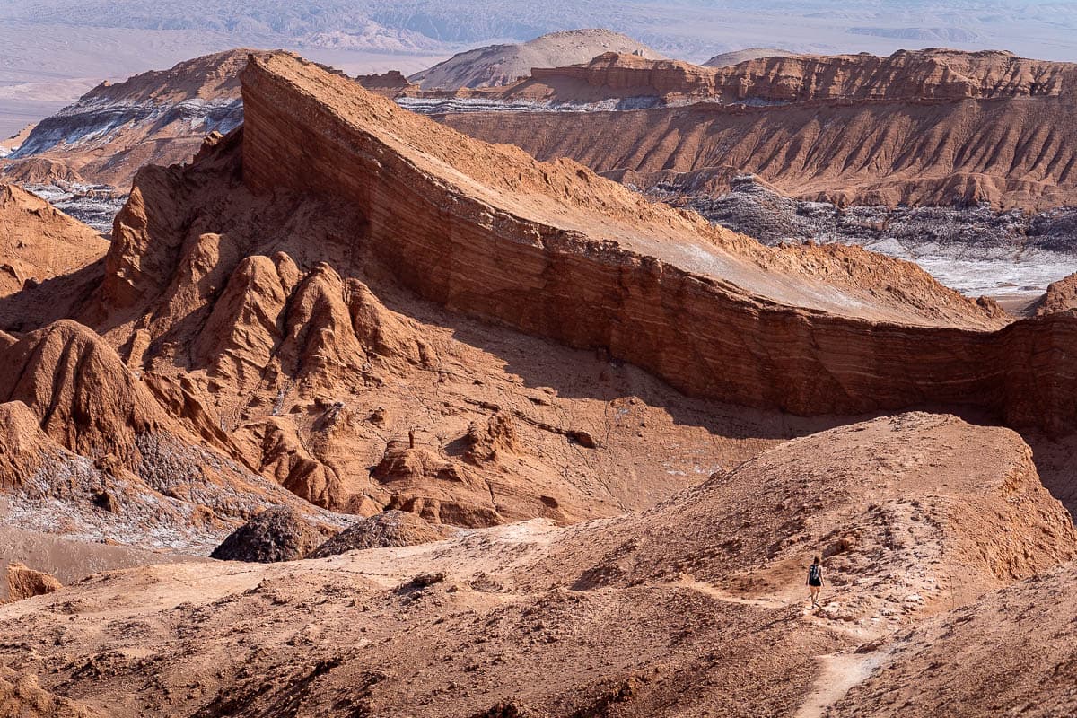 Woman hiking along Sendero Mirador Achaches with the Amphitheater rock formation in the background in San Pedro de Atacama, Chile