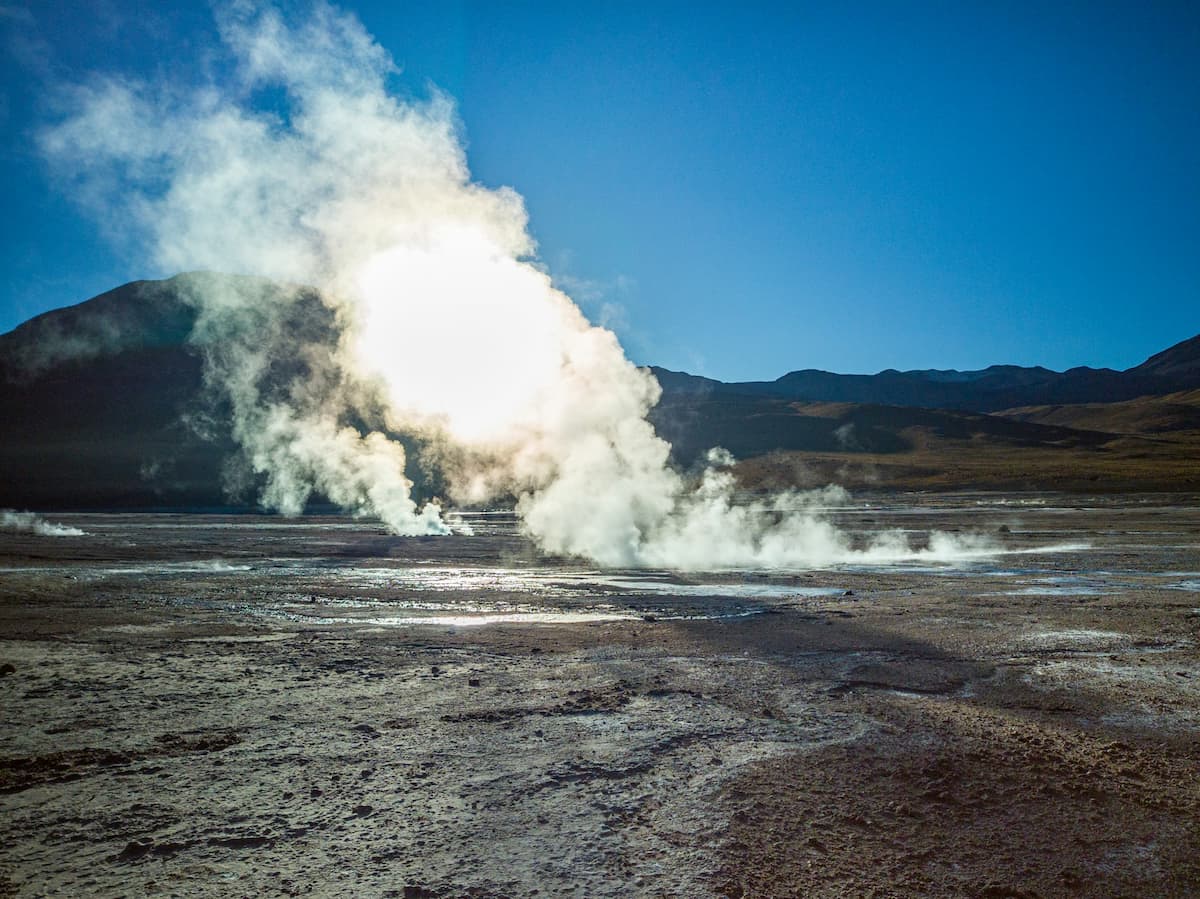 Steam spewing out of El Tatio geysers with mountains in the background in the Atacama Desert, Chile
