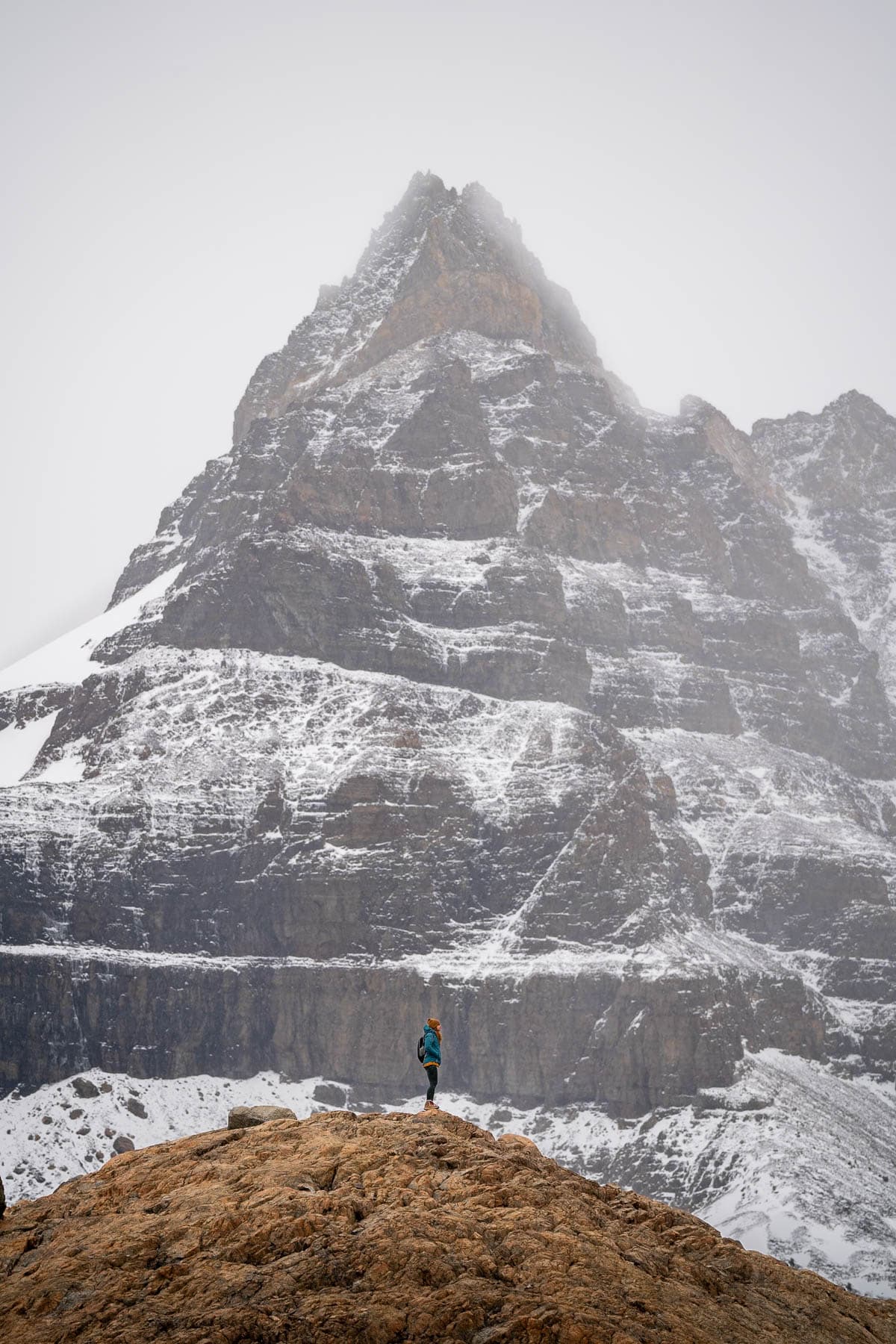 Woman standing on op of a mountain in front of a snowy mountain peak along the Laguna de los Tres trail in El Chalten, Argentina