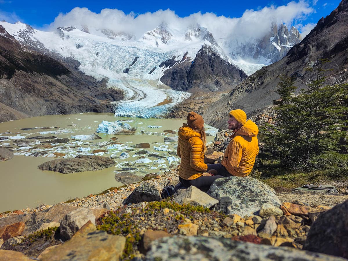 Couple sitting on a rock in front of Glacier Grande spilling down Cerro Torre along the Laguna Torre trail in El Chalten, Argentina
