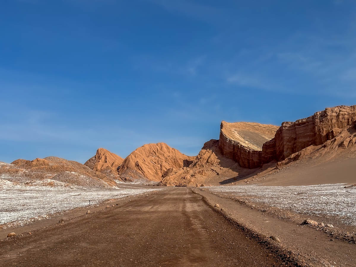 Gravel road leading through Valle de la Luna with rock formations in the background in the Atacama Desert in Chile