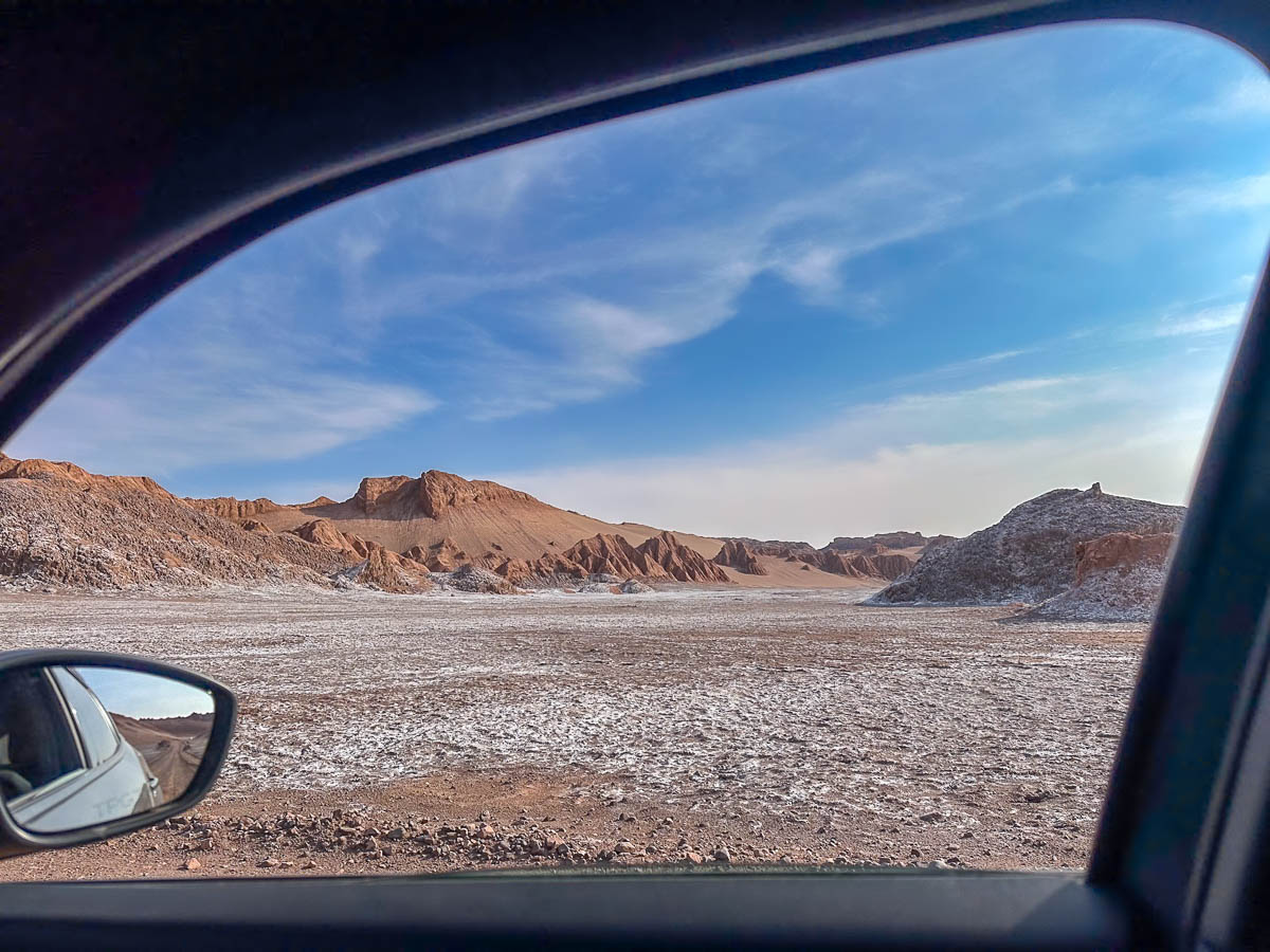View out of car window in the background with mountains and rock formations covered in salt in Valle de la Luna in the Atacama Desert in Chile