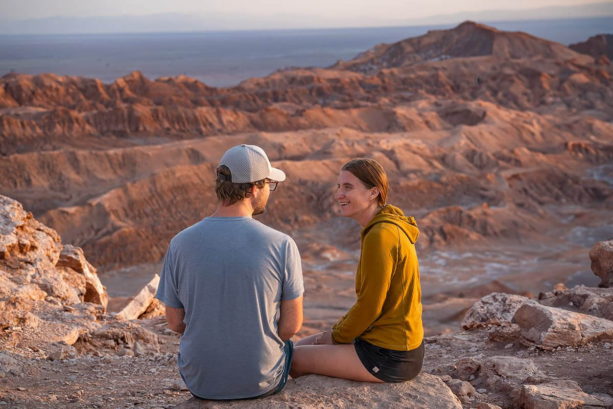 Smiling couple sitting at Mirador de Kari with Valle de la Luna in the background near San Pedro de Atacama in the Atacama Desert, Chile